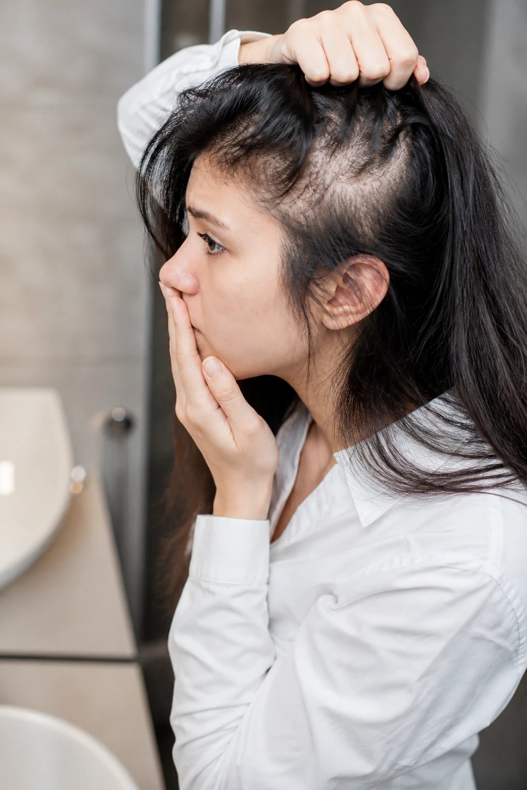 Woman noticing scalp thinning in the mirror — the concern that brings patients to a hair loss consultation